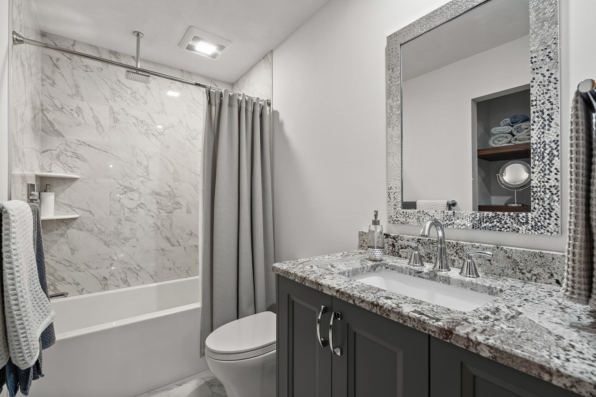 A bathroom featuring a vanity with a granite countertop, a sink, a decorative mirror, a toilet, and a bathtub with a shower.