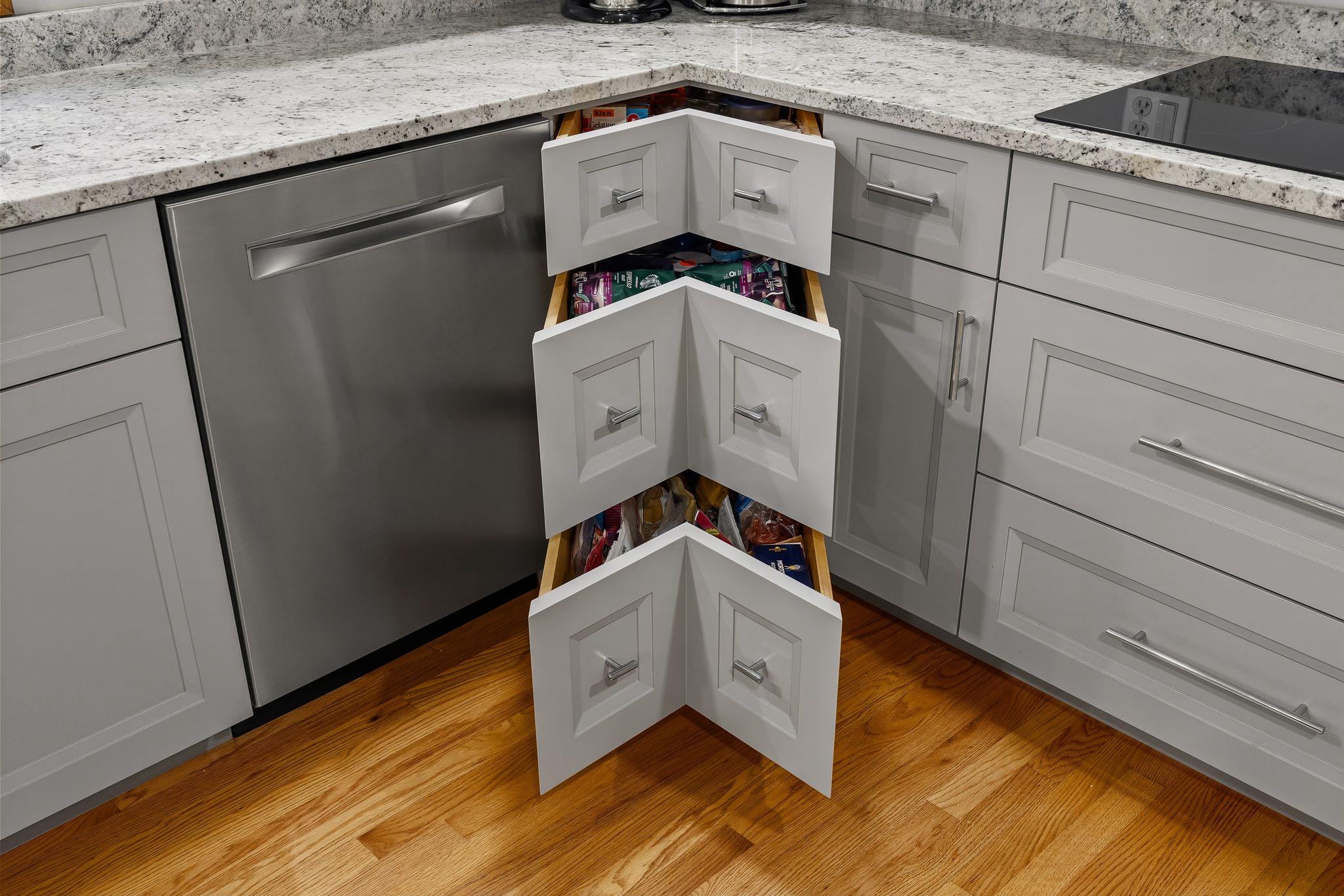 A kitchen features open corner pull-out drawers, a stainless steel dishwasher, and an induction cooktop.