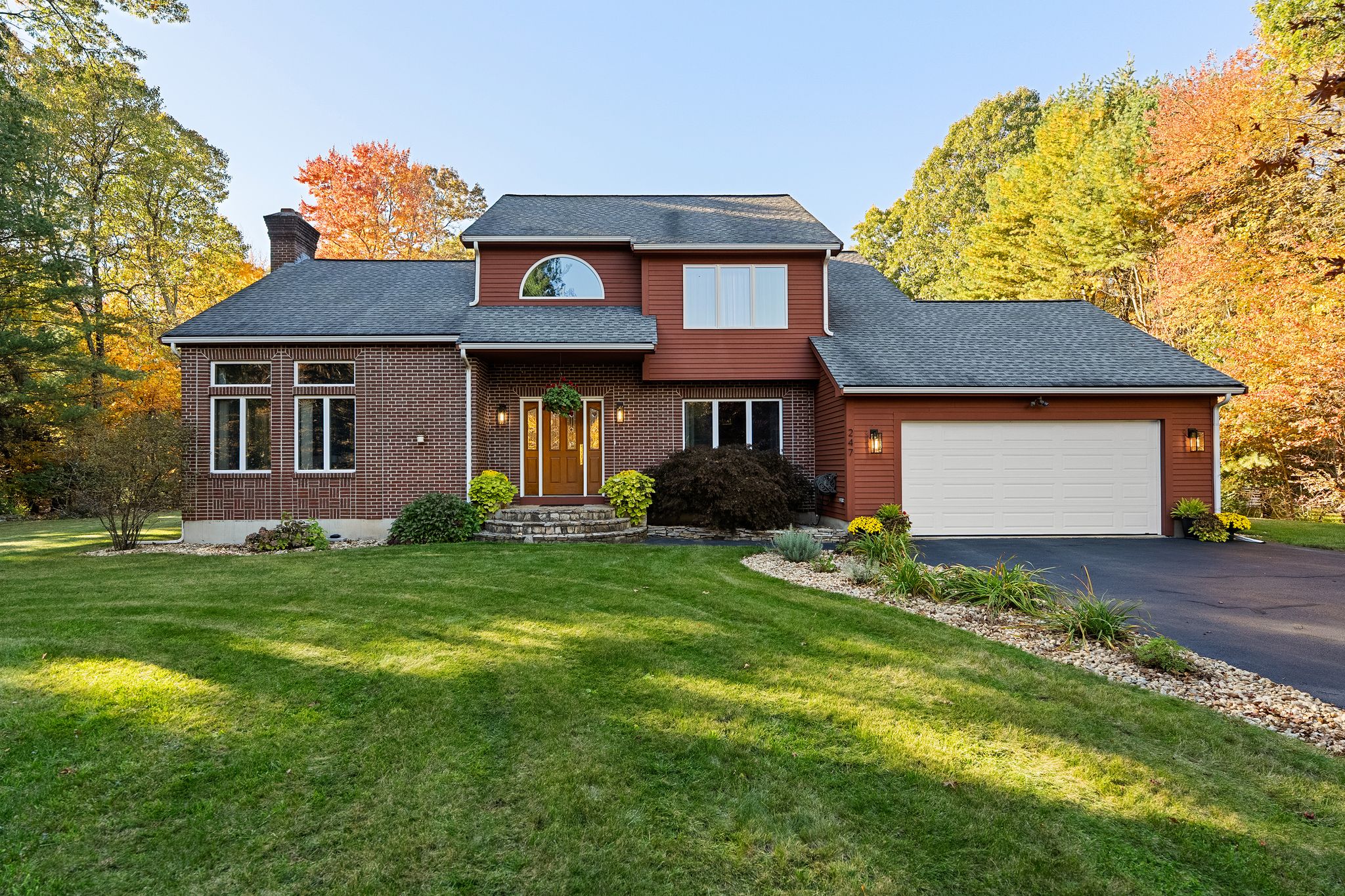 A two-story house with a brick and red siding exterior, a front yard, and a two-car garage, surrounded by fall foliage.