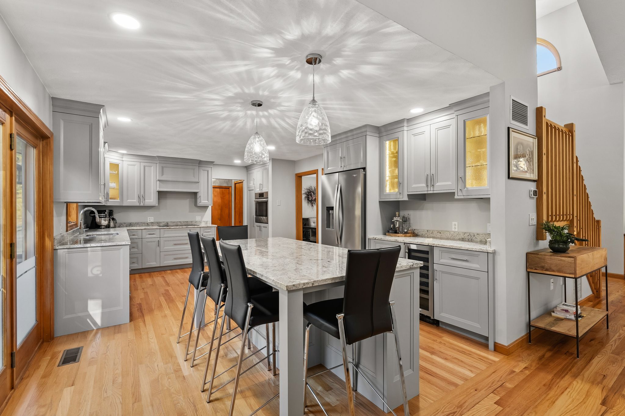 A modern kitchen features gray cabinetry, a large island with seating, stainless steel appliances, and hardwood floors.