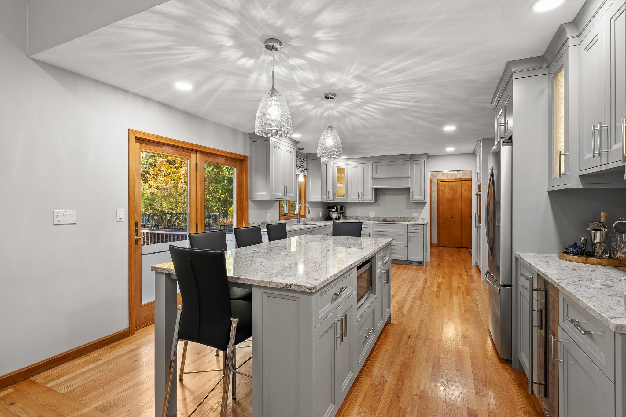 A kitchen features light gray shaker cabinets, a large island with seating, and hardwood floors.