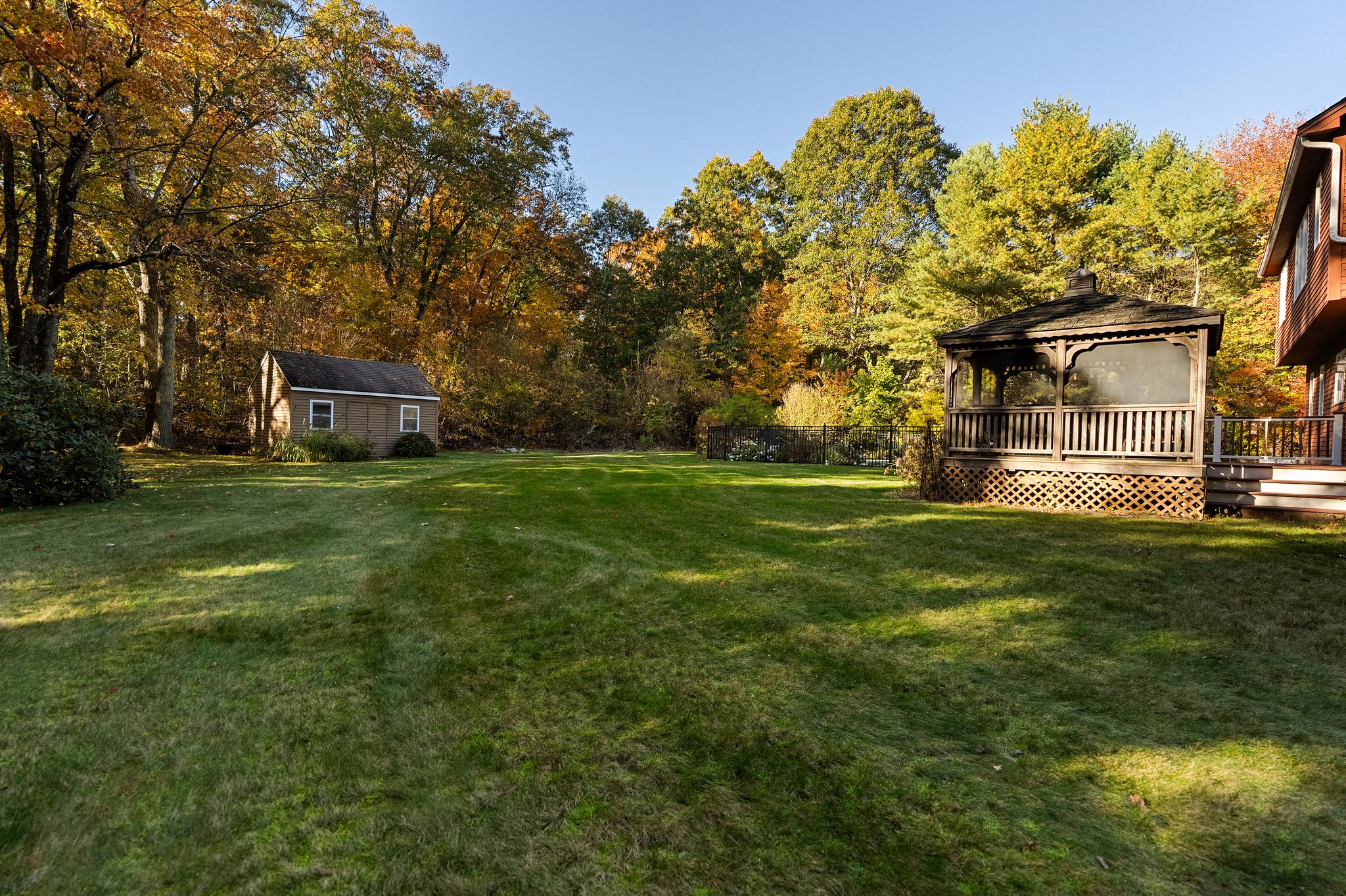 A spacious backyard with a shed, a gazebo, and colorful fall foliage.