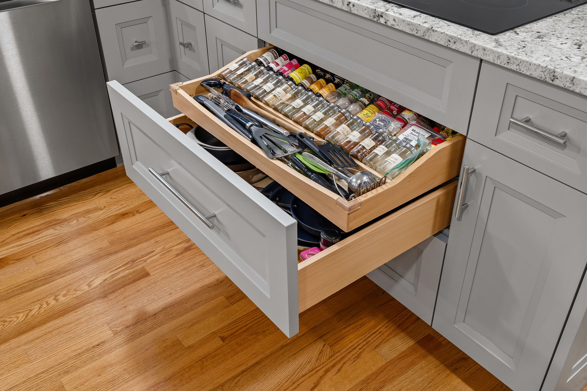 An open kitchen drawer showcases an organized spice rack and cooking utensils in a grey cabinet.