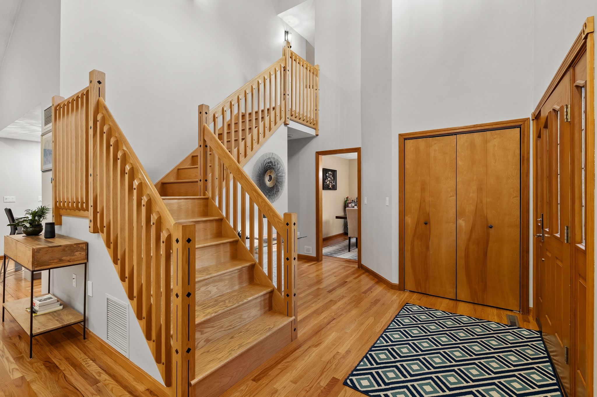 A bright entryway features a wooden staircase, hardwood floors, and a console table.