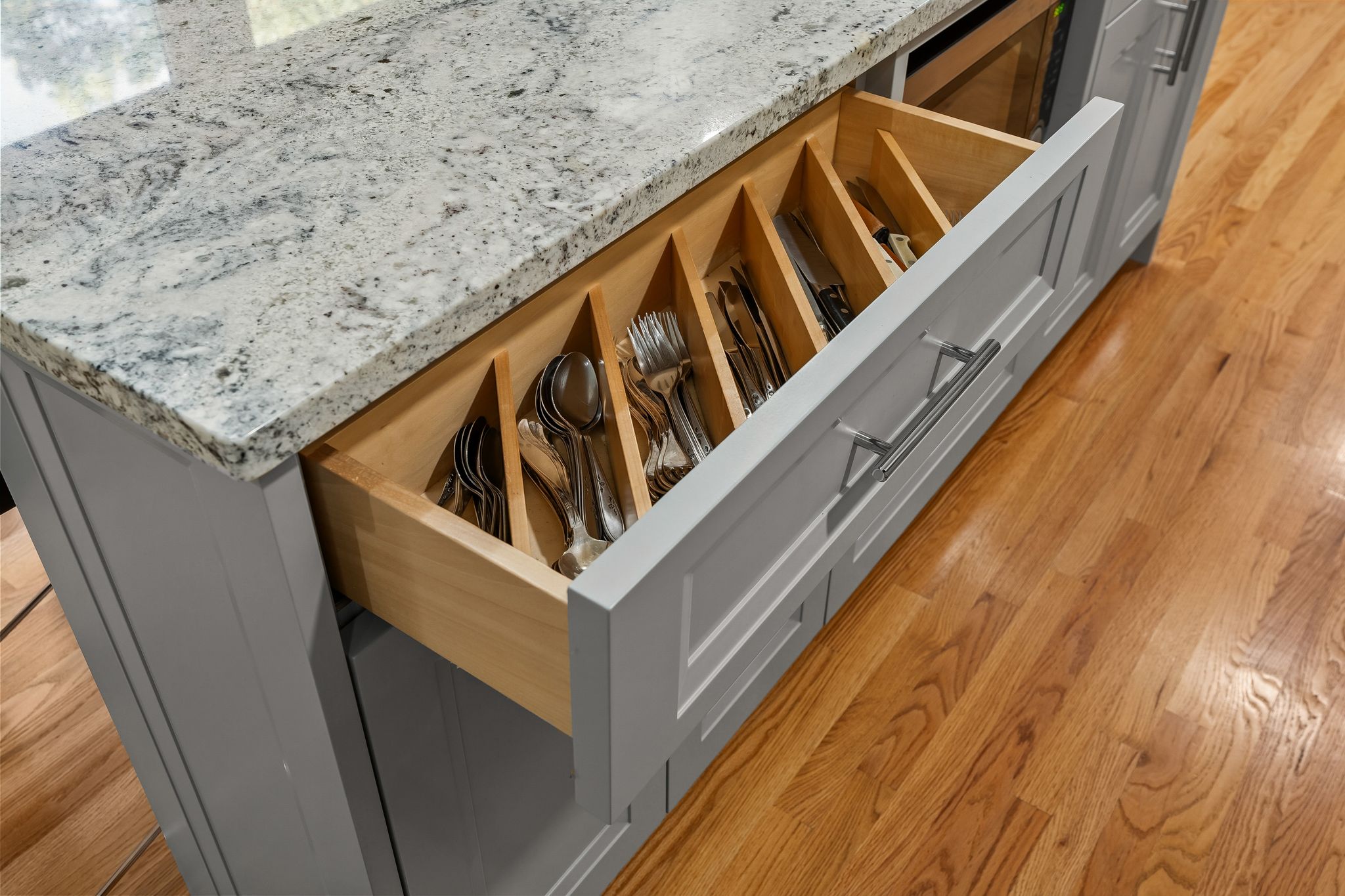 A kitchen island with a granite countertop features an open drawer with organized cutlery.