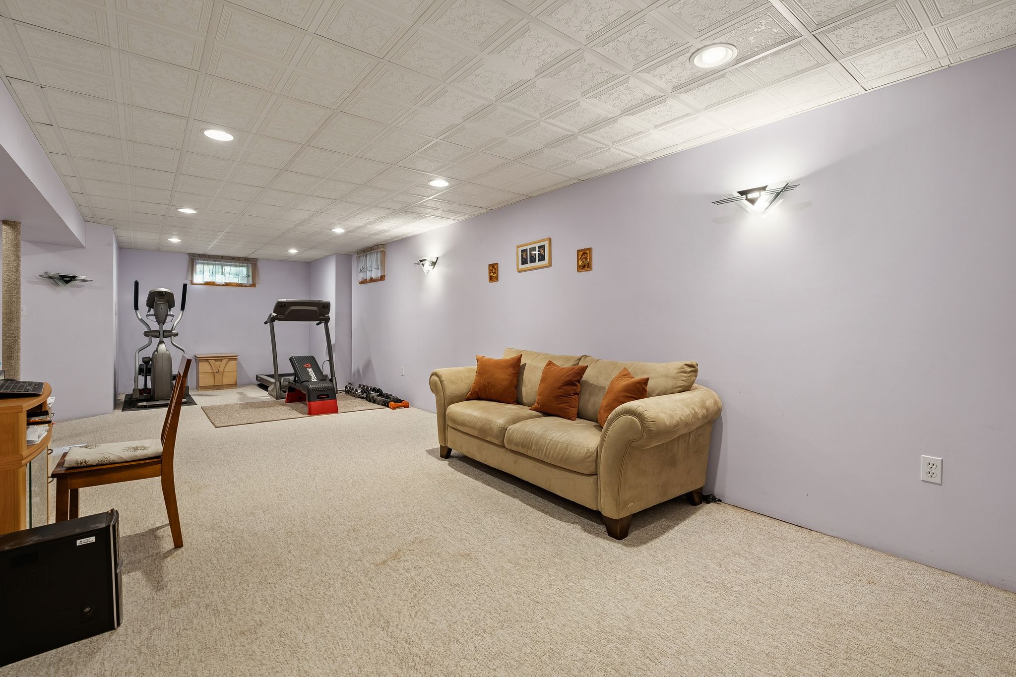 A basement room with a sofa, exercise equipment, a desk, and carpeted floors.