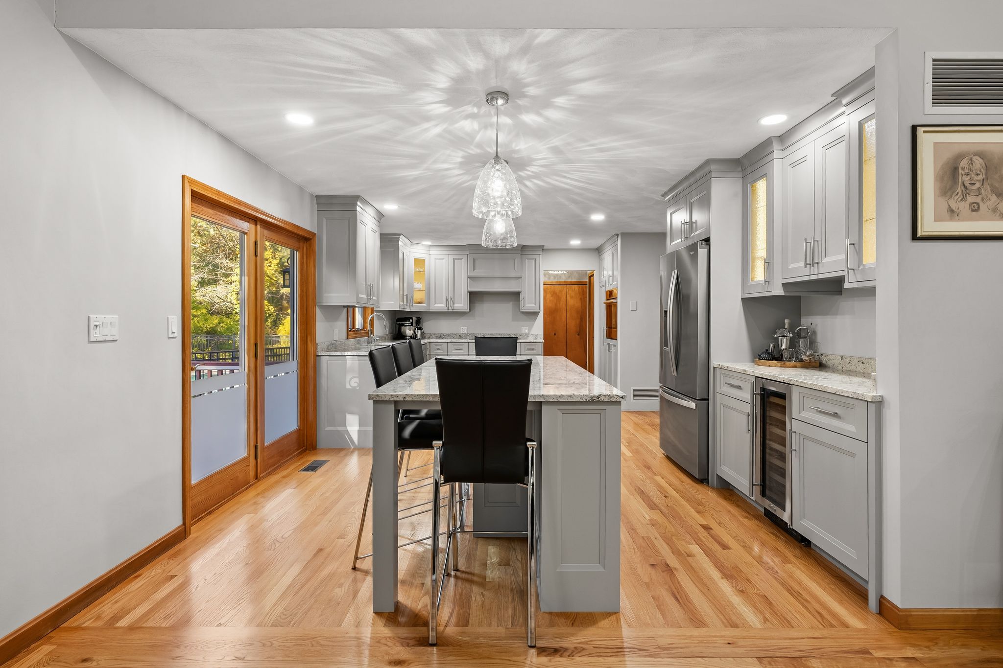 An interior view of a kitchen featuring light grey cabinetry, an island with bar stools, and stainless steel appliances.