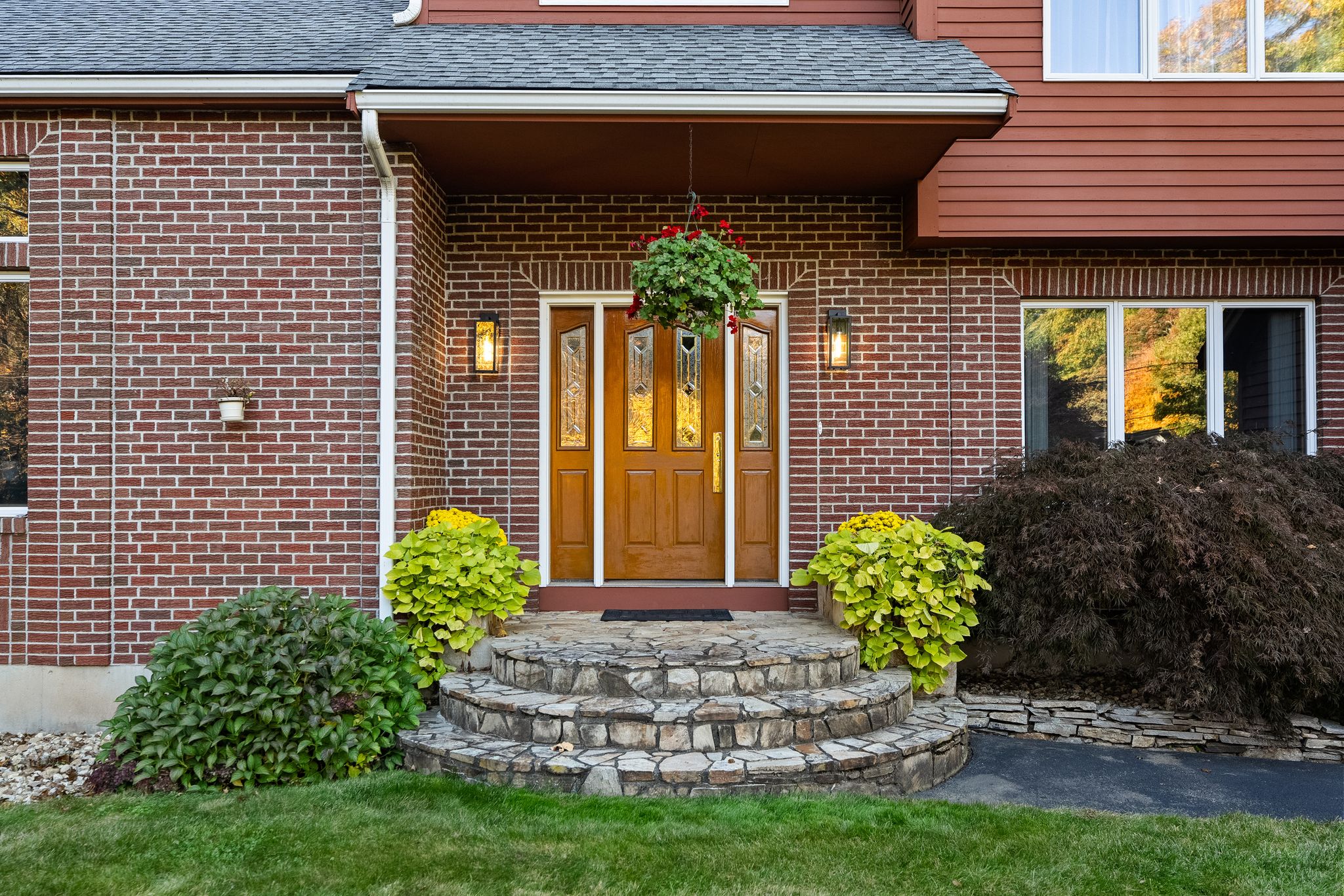The front entrance of a brick house features a wooden door, stone steps, and potted plants.